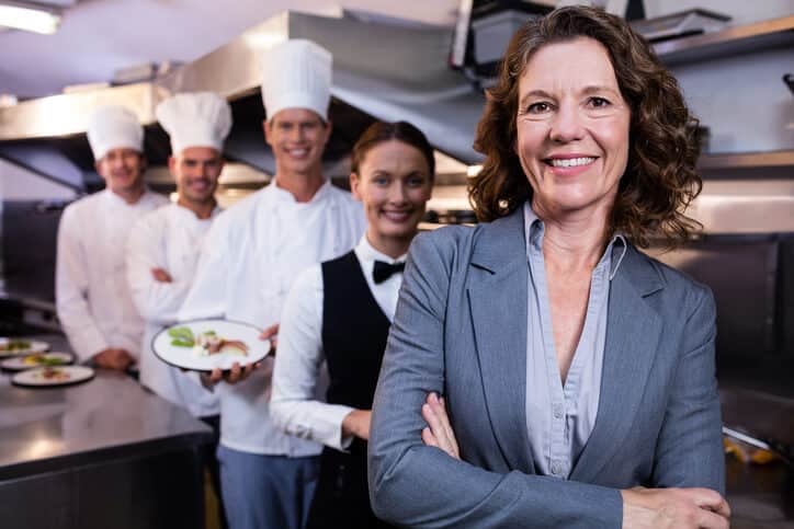 A smiling female food service manager with a group of chefs after completing her food and nutrition management diploma