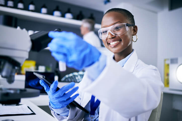 A smiling female pharma QA professional holding a sample in a laboratory